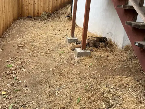 Bare ground under a wooden deck and its stairs beside a fence, the dry grass and brush cleared away